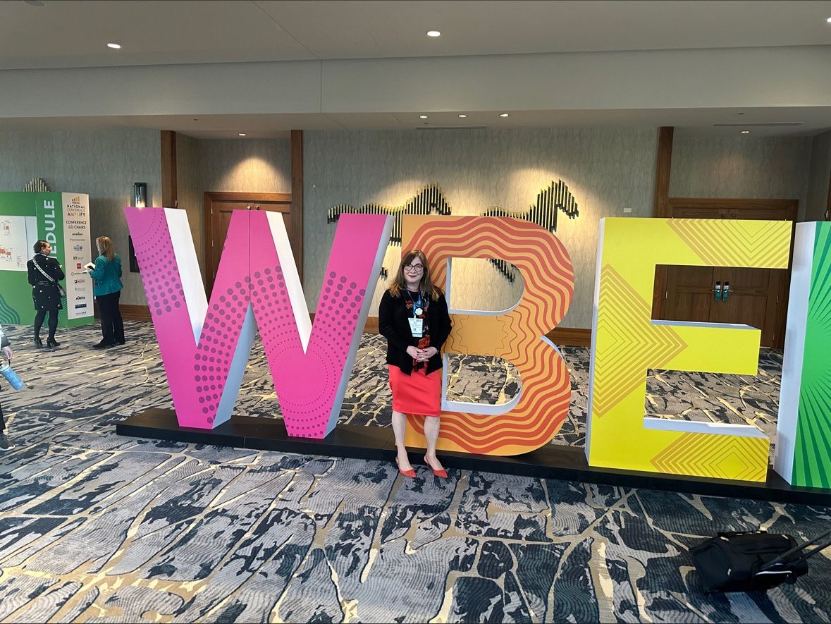 Darcy Ann Flanders at the 2024 WBENC National Conference in Denver, standing in front of a large "WBEC" sign
